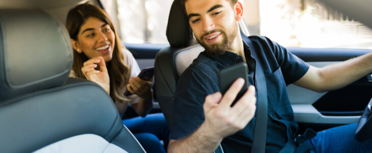 Male rideshare driver communicating with female passenger in backseat of car