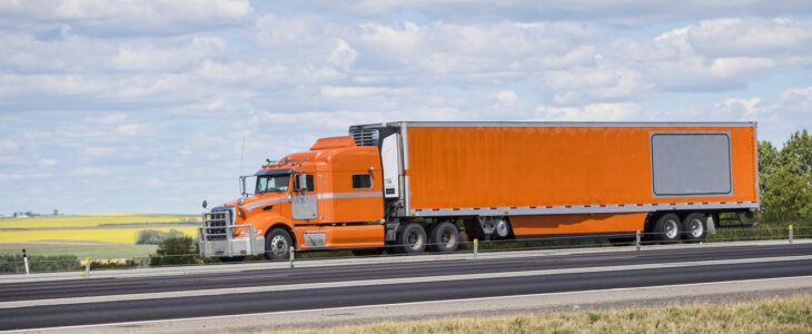 An orange truck carrying cargo down a highway