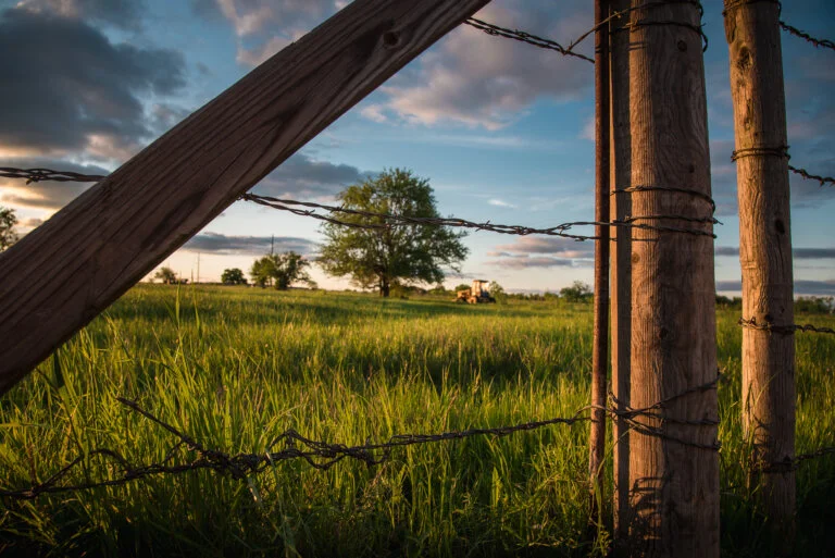 Bryan TX Ranch and Tractor Seen Through Barbed Wire Fence at Sunset