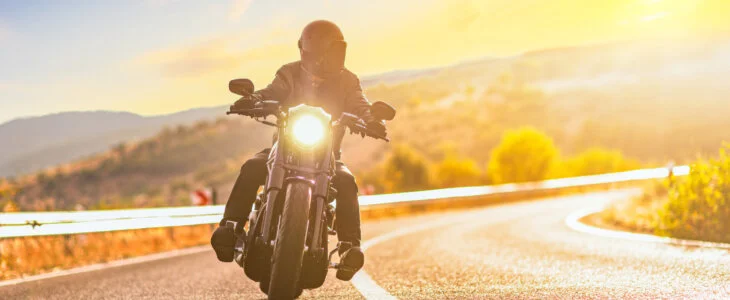 Sunset over an open road and a man with a helmet riding a motorcycle