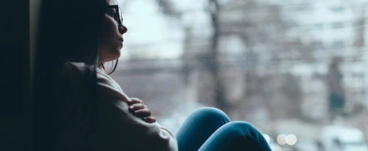 Silhouette of sad teenage girl looking out the window on a cold autumn day