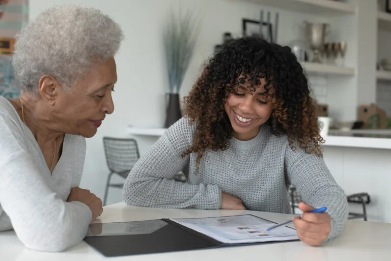 Advisor and client smiling while reviewing forms together at a home kitchen table