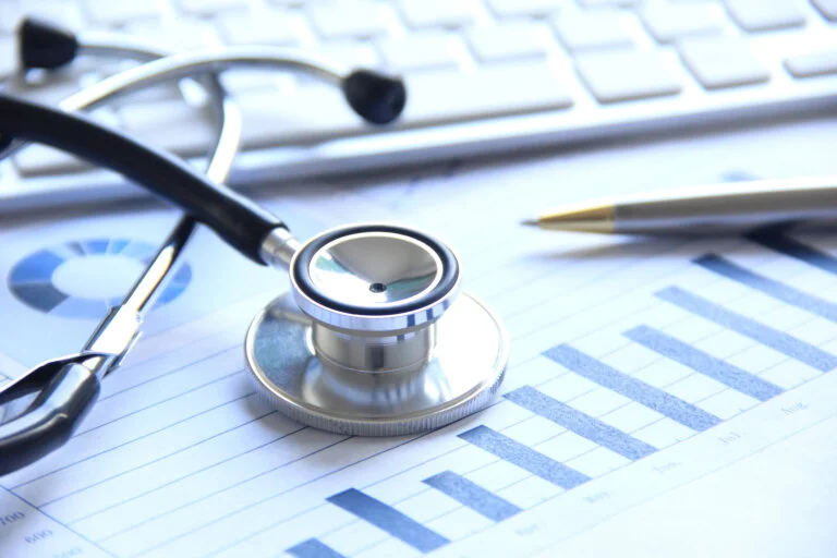 Stethoscope on financial charts beside pen and keyboard