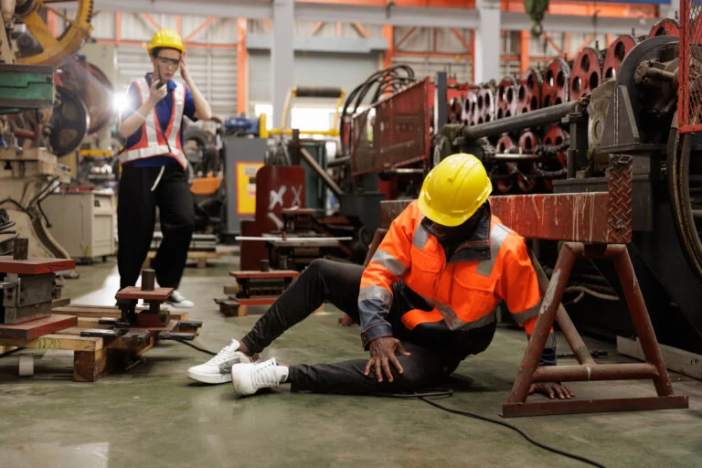 Industrial accident scene showing a worker sitting on the floor in pain